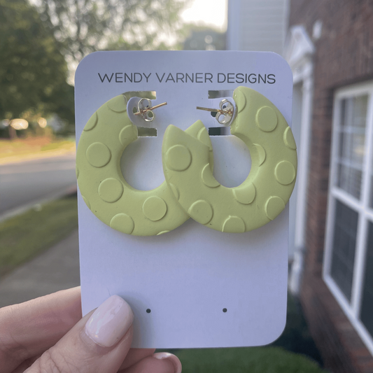 Close-up of circular chartreuse earrings with polka dot texture, displayed on an earring card outdoors.