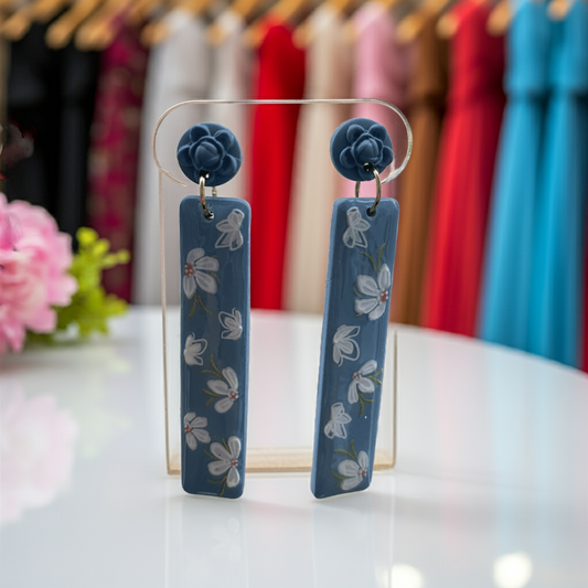 Close-up of blue floral polymer clay dangle earrings handmade in Charlotte NC shown on display in a boutique.