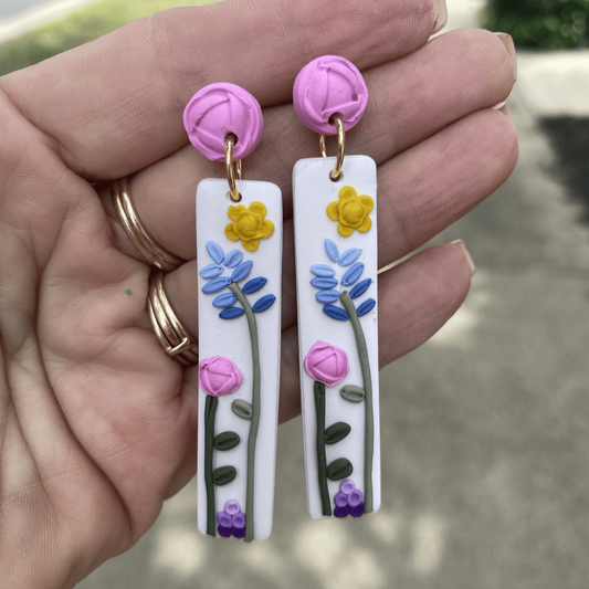 Close-up of handmade floral earrings held in hand showing texture, colors, and detailed