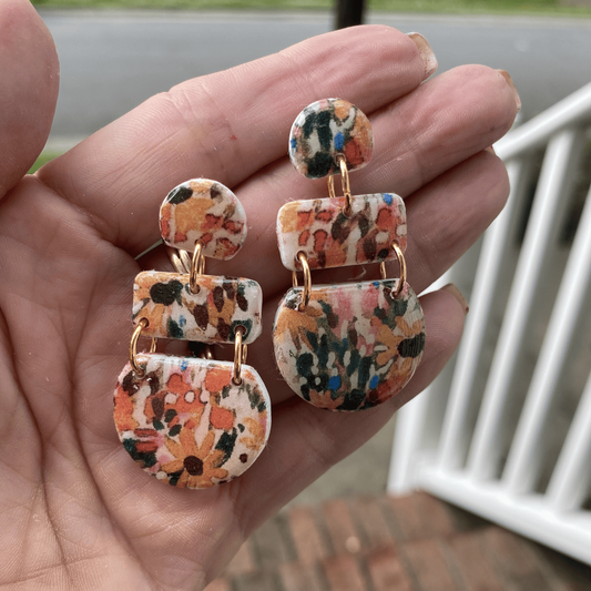 Close-up of floral polymer clay dangle earrings held in hand, featuring warm-toned abstract flower patterns