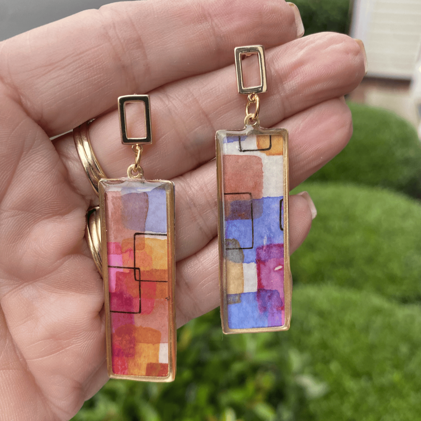 Close-up of handmade abstract watercolor framed earrings held in hand