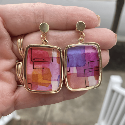 Close-up of handmade abstract watercolor framed earrings held in hand