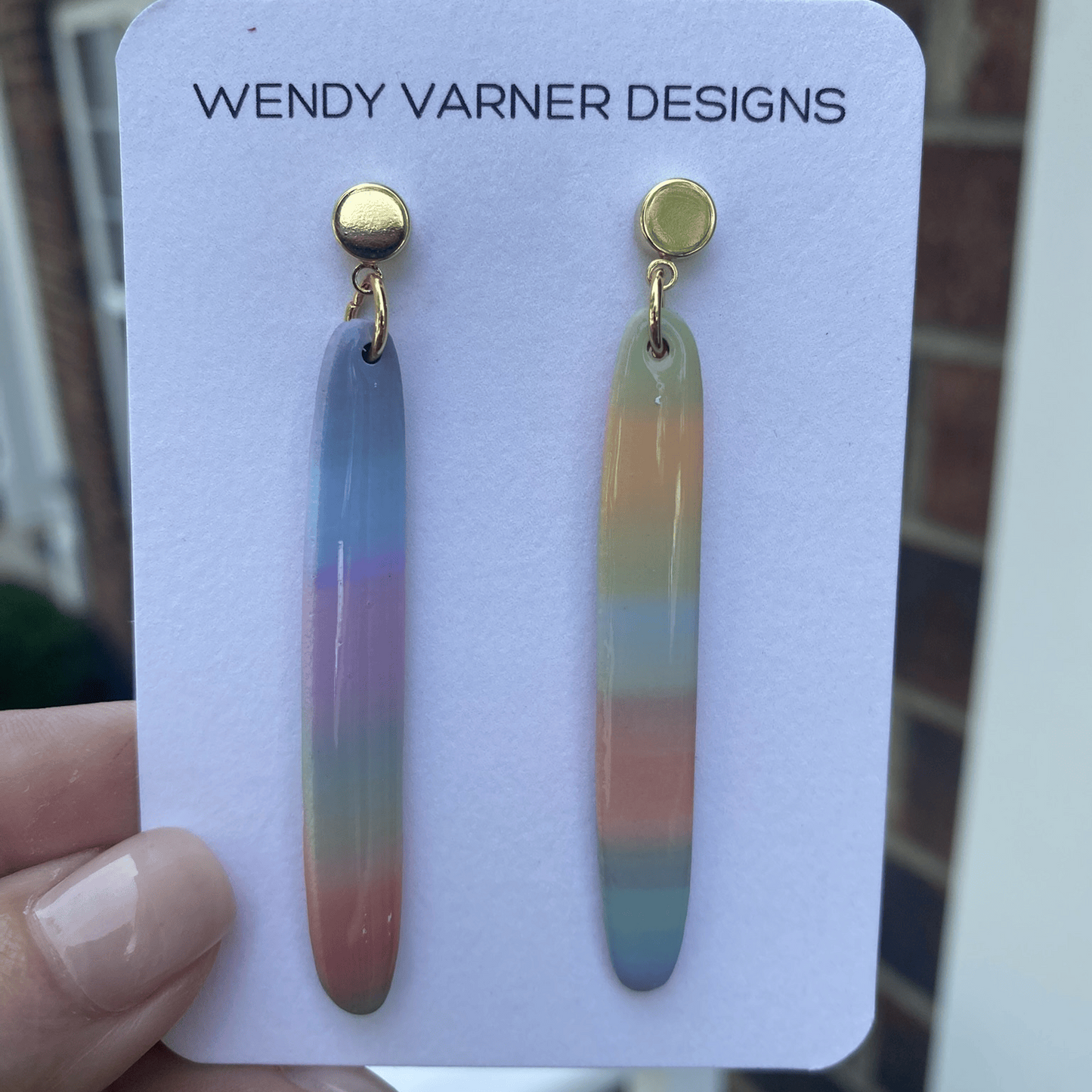 Handmade pastel rainbow stripe polymer clay earrings on white display card by Wendy Varner Designs, photographed outdoors in Charlotte NC.