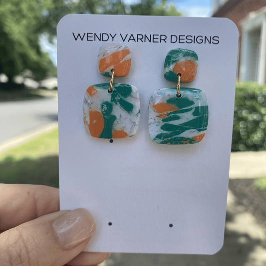 Vibrant handmade earrings held outdoors on sunny Charlotte sidewalk