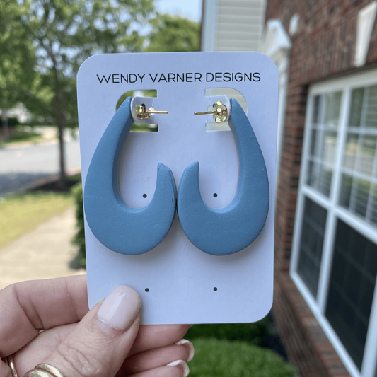 Teardrop-shaped blue polymer clay earrings held outdoors, handcrafted in Charlotte North Carolina