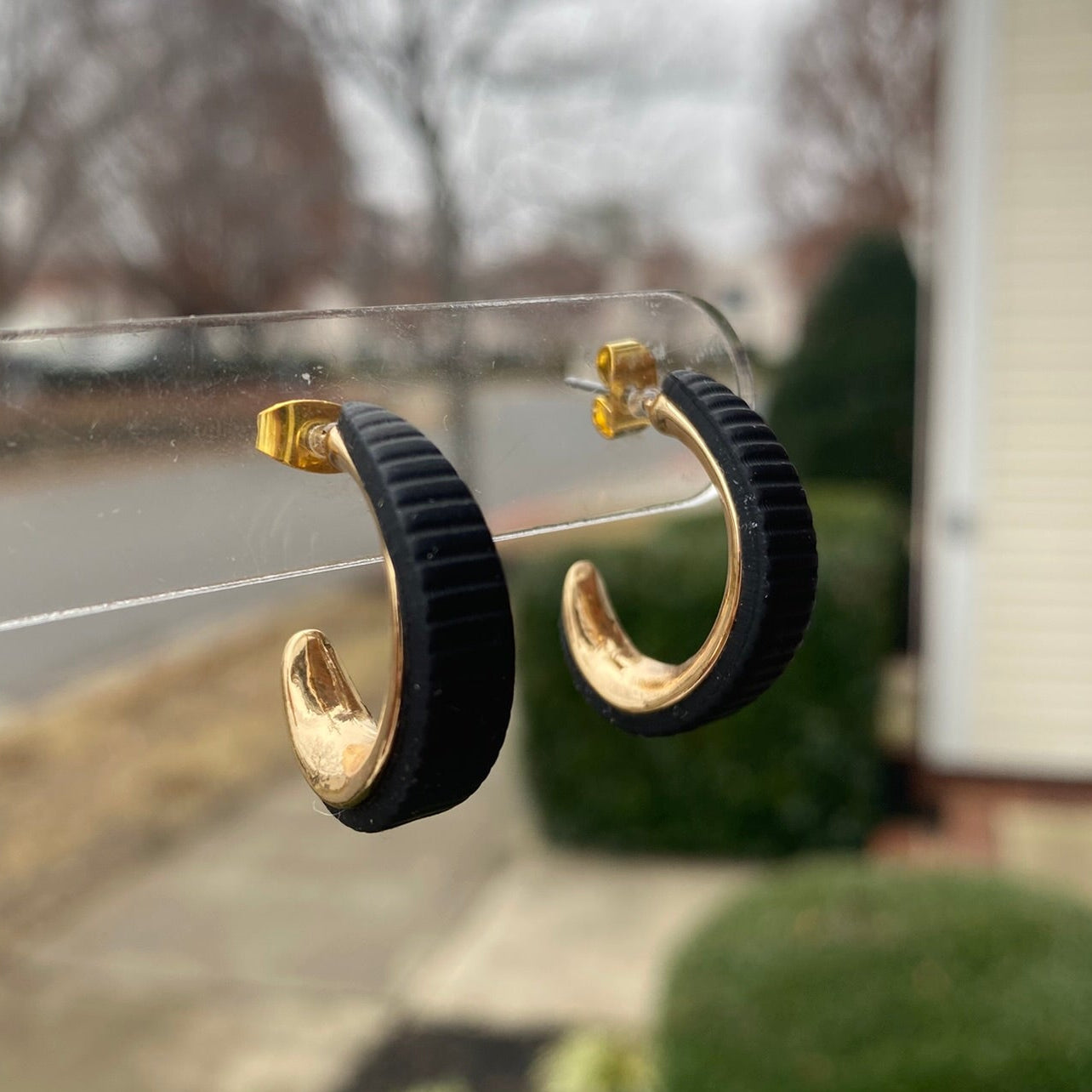 Black and gold polymer clay hoop earrings displayed outdoors on clear stand, handmade by Wendy Varner Designs