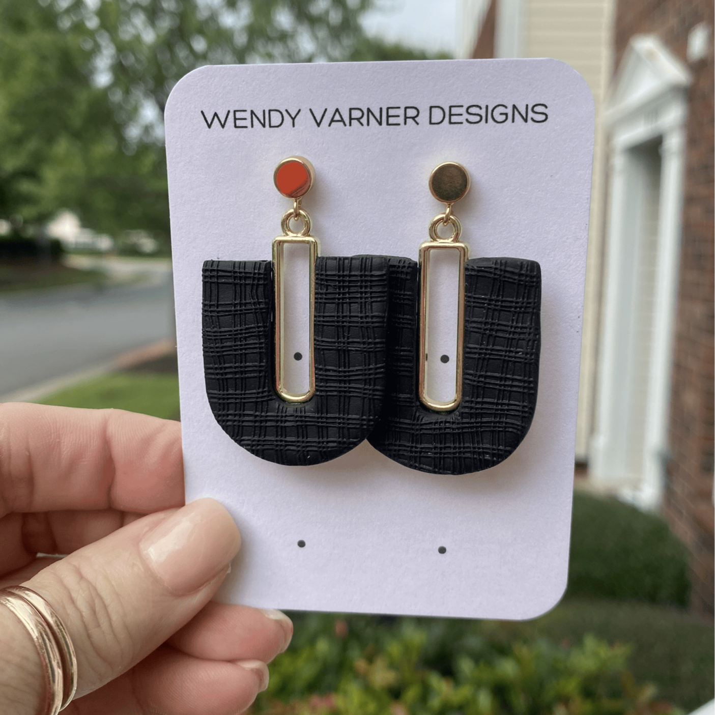 Close-up view of black plaid textured polymer clay earrings with gold-plated rectangle accent and gold post top.