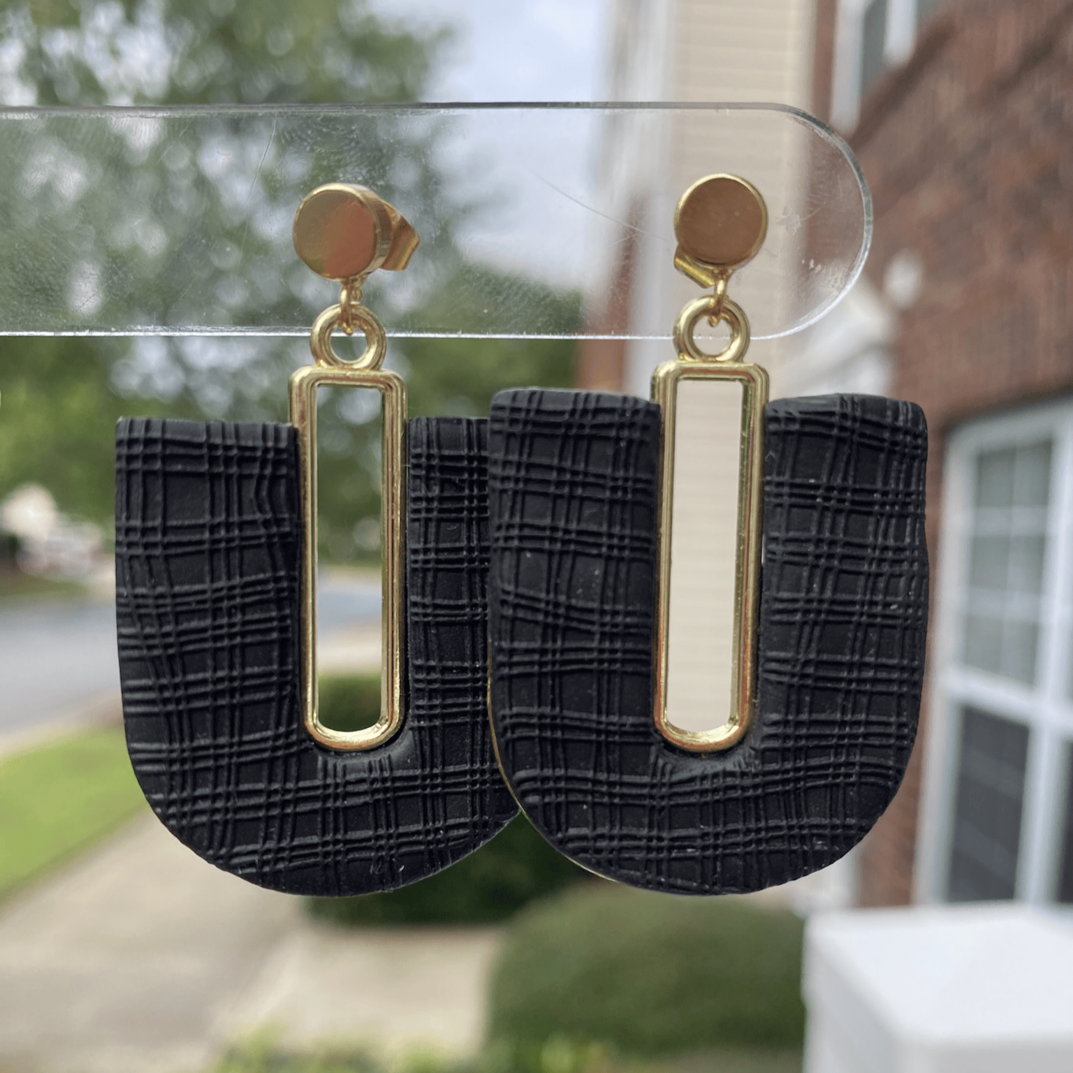 Black plaid textured polymer clay arch earrings with gold-plated open rectangle accent, hanging display.