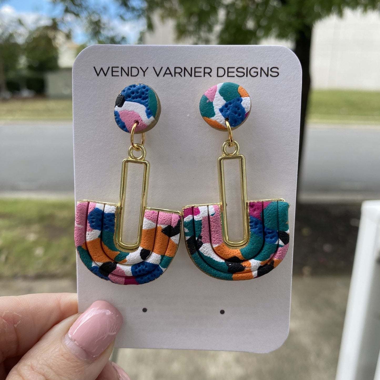 Close-up of handmade polymer clay earrings featuring pink, teal, orange, black, and blue pattern