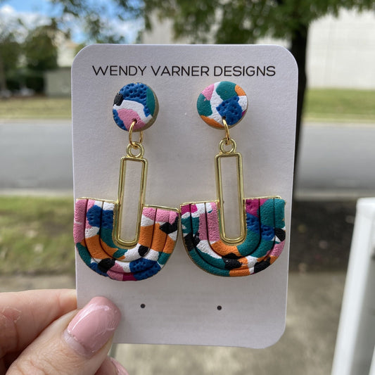 Close-up of handmade polymer clay earrings featuring pink, teal, orange, black, and blue pattern