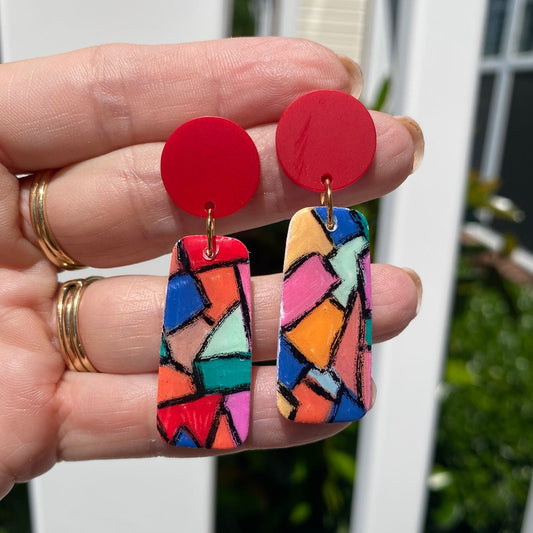 Close-up of hand-painted polymer clay stained glass mosaic dangle earrings held in hand, showing vibrant multicolor geometric pattern, handcrafted by a small maker in Charlotte NC