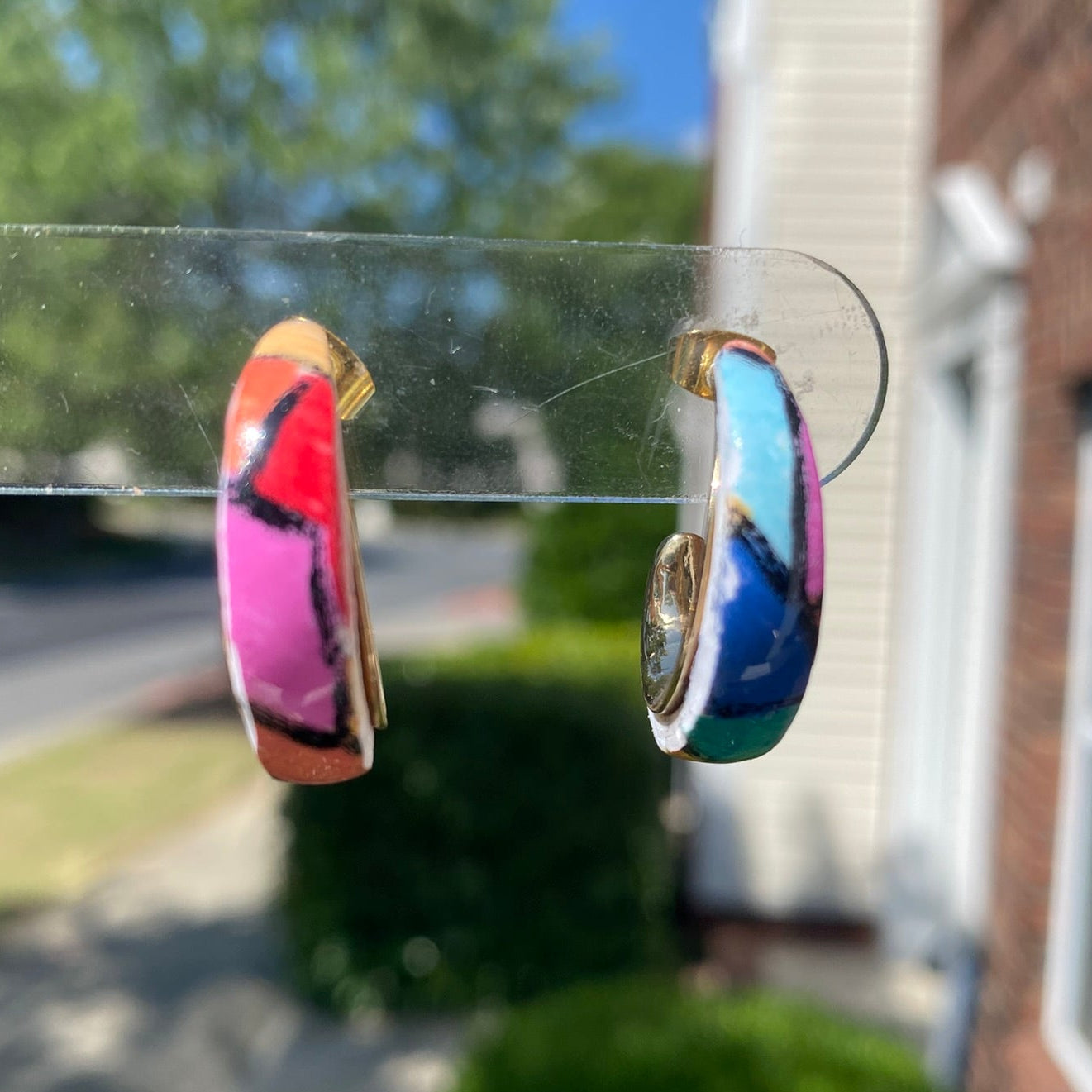 Pair of hand-painted polymer clay stained glass mosaic hoop earrings on a clear display stand, showing vibrant pink, magenta, blue and teal mosaic pattern, handcrafted in Charlotte NC