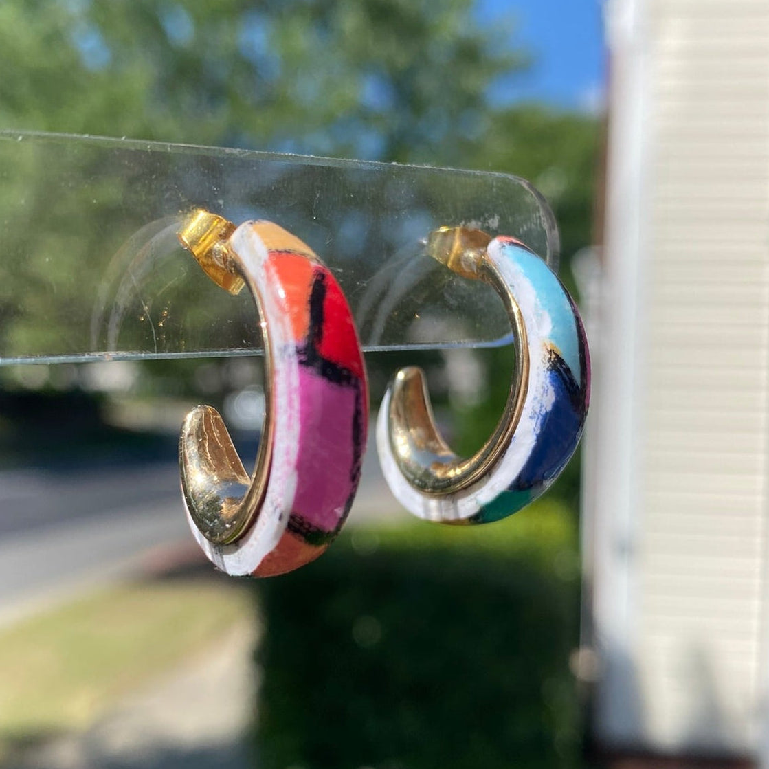 Side view of hand-painted polymer clay stained glass mosaic hoop earrings on a clear display stand, showing full hoop shape with multicolor mosaic detail, handmade in Charlotte NC