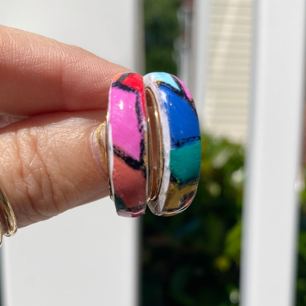 Pair of hand-painted polymer clay stained glass mosaic hoop earrings held in hand showing vibrant pink, blue, teal, red and white pattern, handcrafted in Charlotte NC