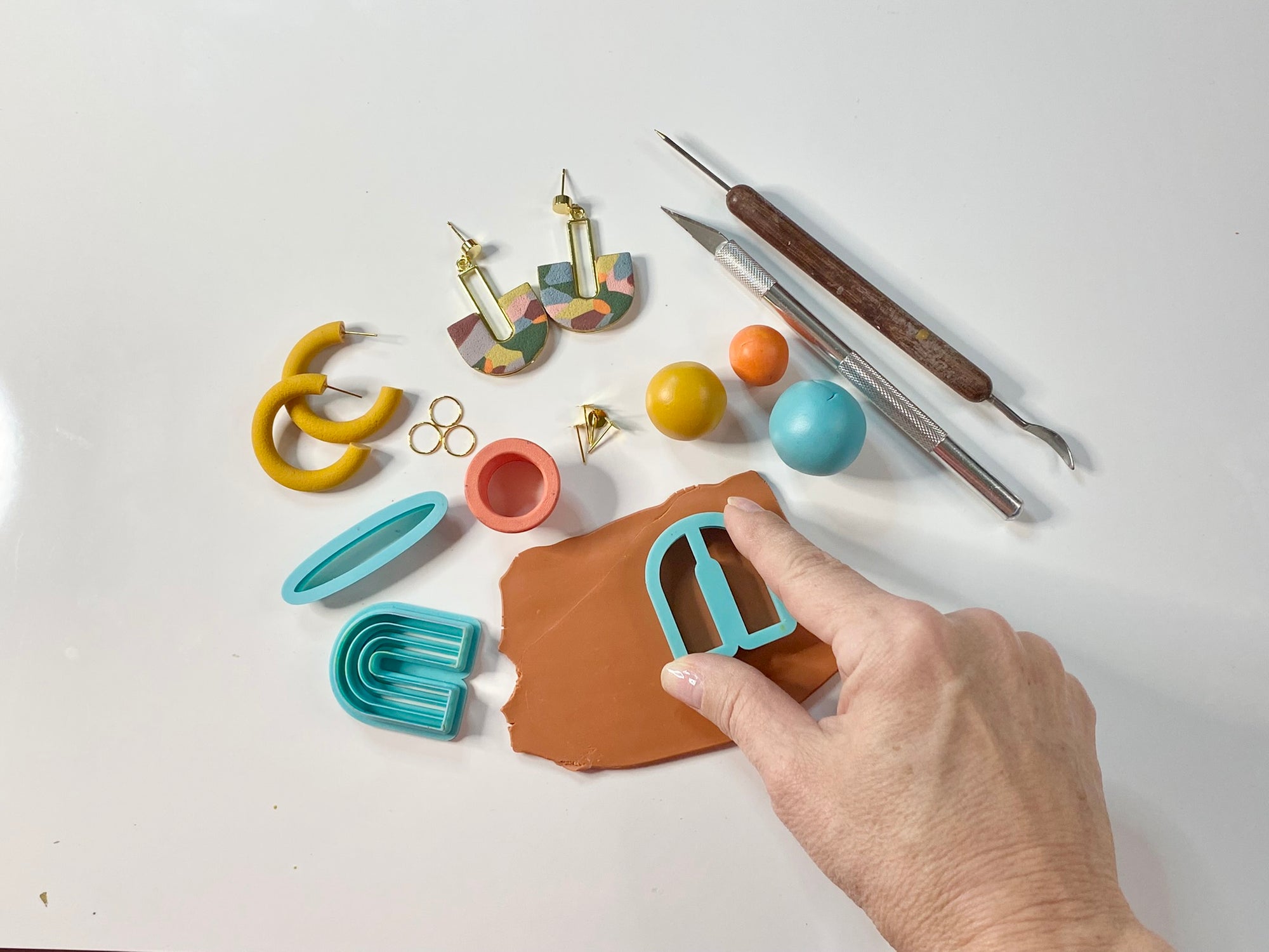 Handcrafting colorful polymer clay earrings with DIY tools, cutters, and accessories on a white background"