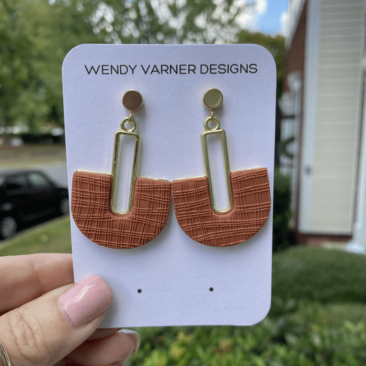 Terracotta polymer clay arch earrings with gold rectangle accent, displayed outdoors.