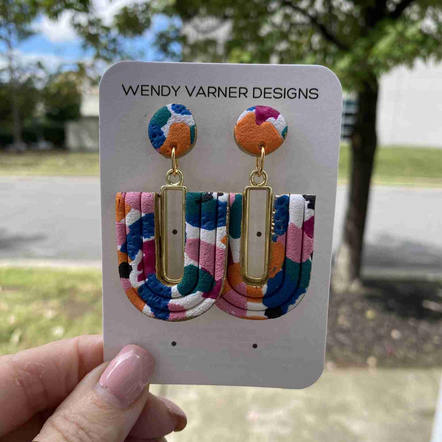 Close-up of colorful U-Loop polymer clay earrings with gold bar accent