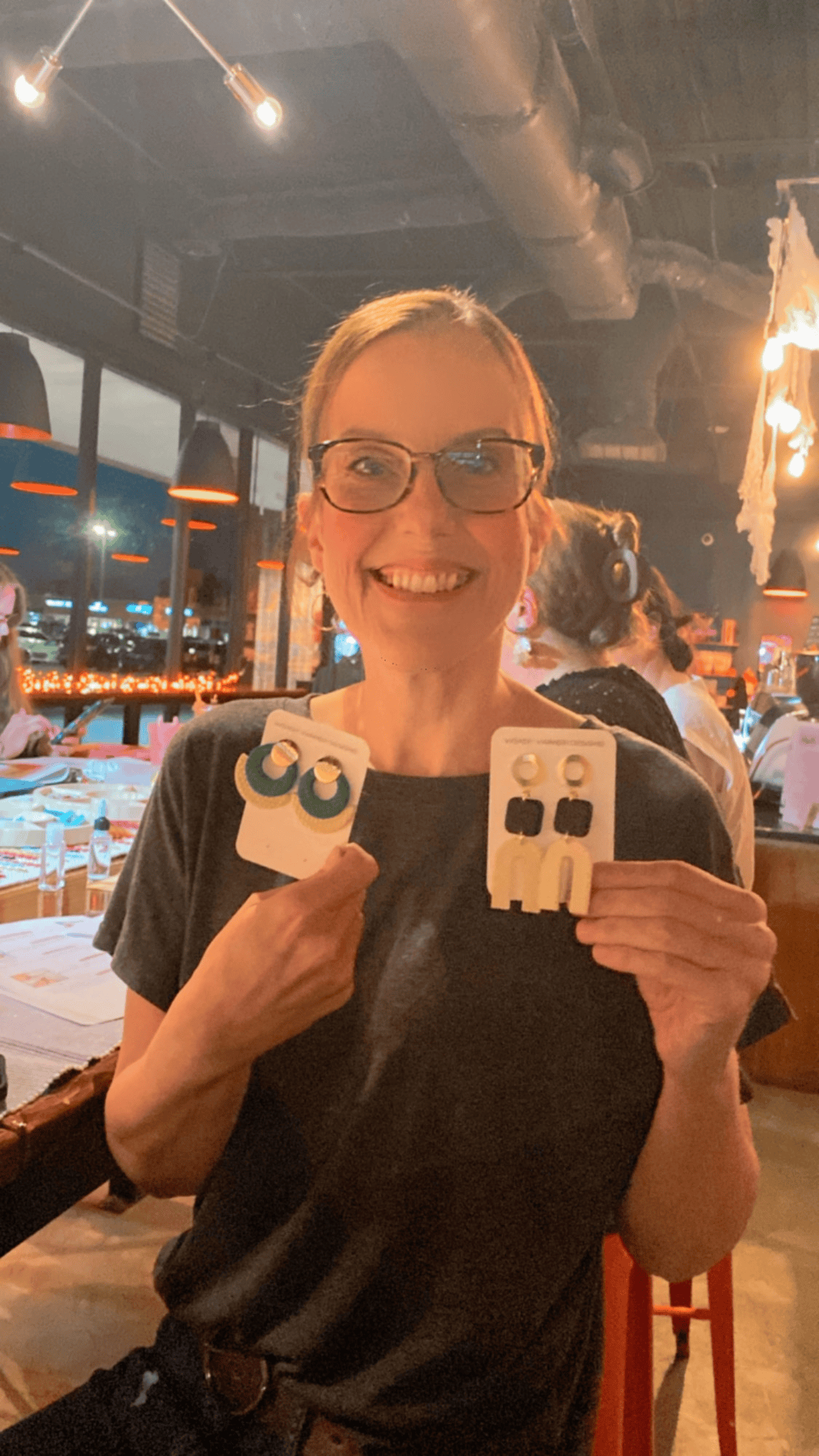 Happy workshop participant holding up two bold and creative pairs of polymer clay earrings.