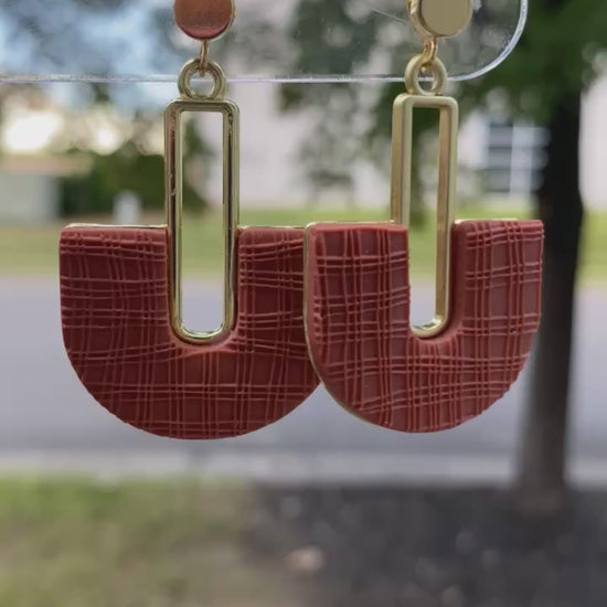 Terracotta polymer clay arch earrings with gold rectangle accent, displayed outdoors.