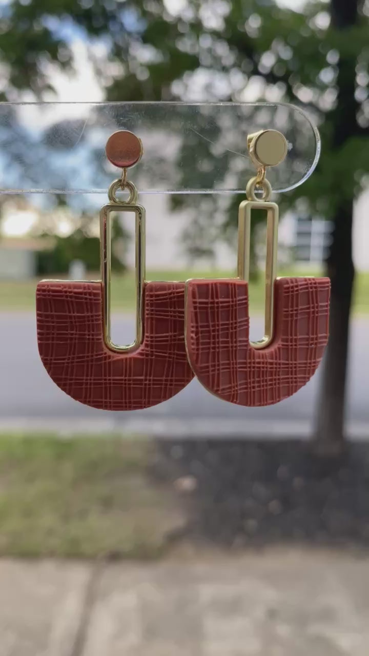 Terracotta polymer clay arch earrings with gold rectangle accent, displayed outdoors.