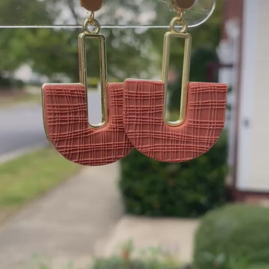 Closeup of terracotta arch polymer clay earrings with textured detail and gold rectangle.