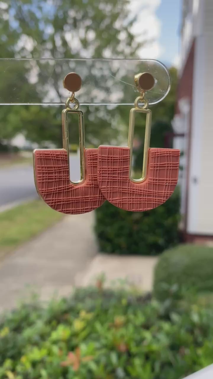 Closeup of terracotta arch polymer clay earrings with textured detail and gold rectangle.