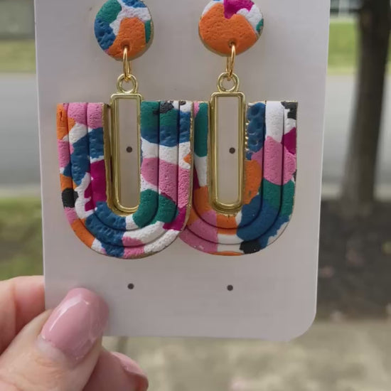Close-up of colorful U-Loop polymer clay earrings with gold bar accent