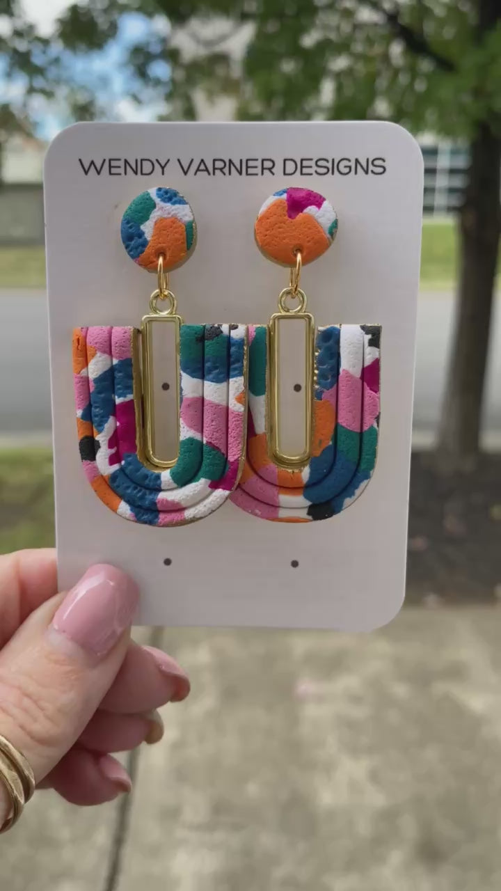 Close-up of colorful U-Loop polymer clay earrings with gold bar accent
