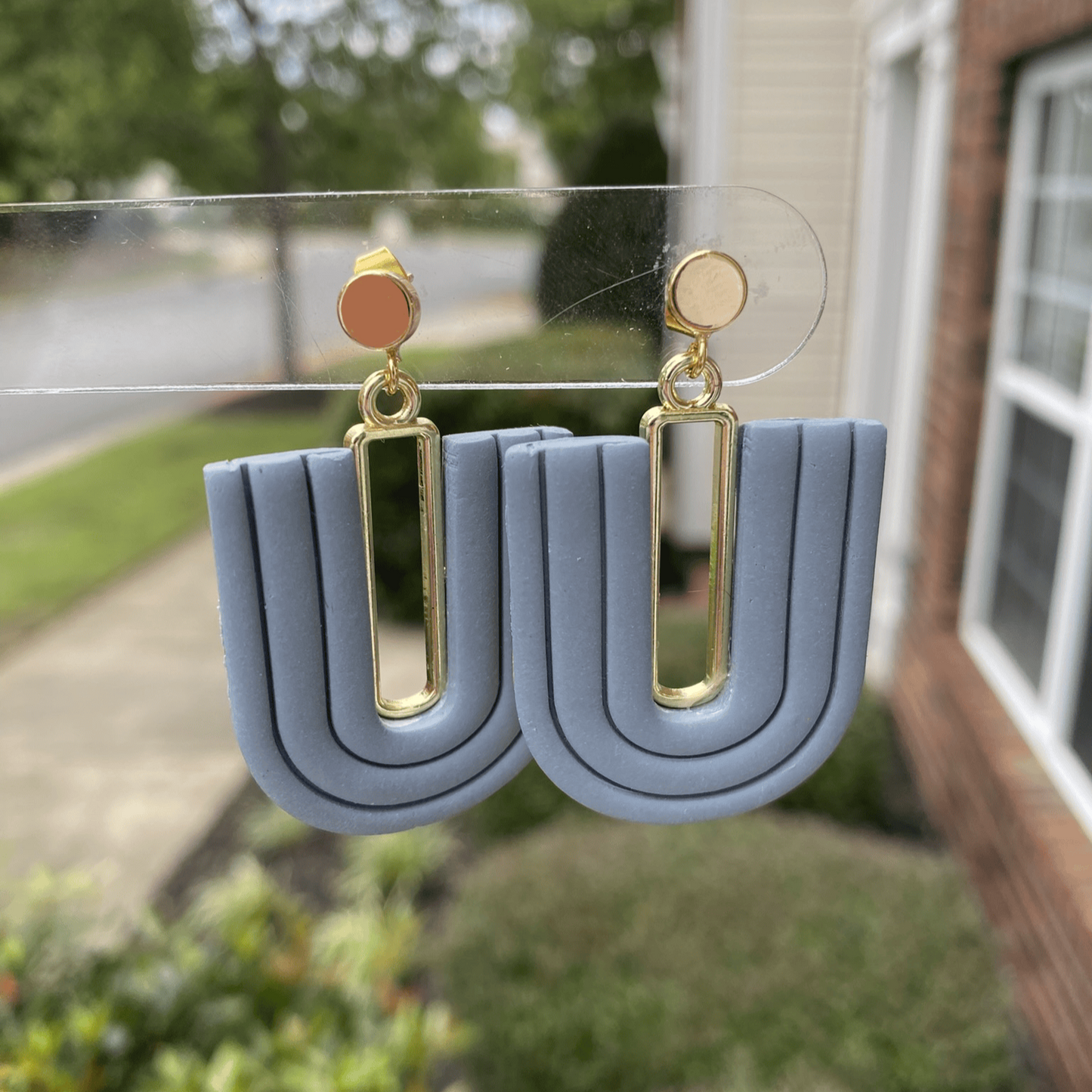 Close-up of steel blue polymer clay statement earrings with layered U-shape and gold-plated accent.