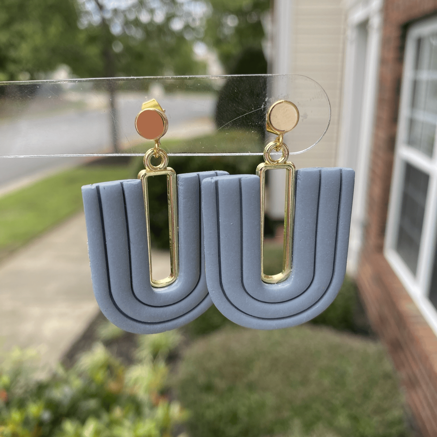 Close-up of steel blue polymer clay statement earrings with layered U-shape and gold-plated accent.