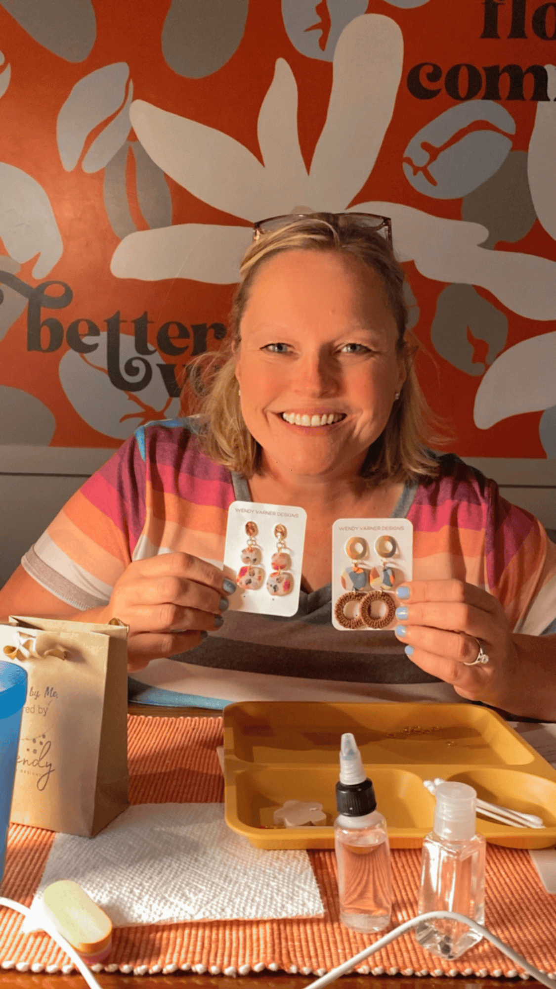 Smiling guest holding two pairs of handmade polymer clay earrings with floral and textured details.